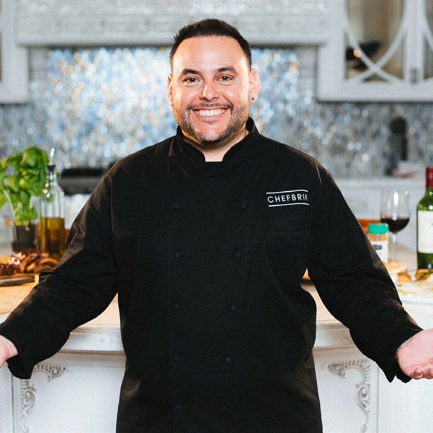 Chef Eddie Brik in his black CHEFBRIK chef coat, smiling in a kitchen